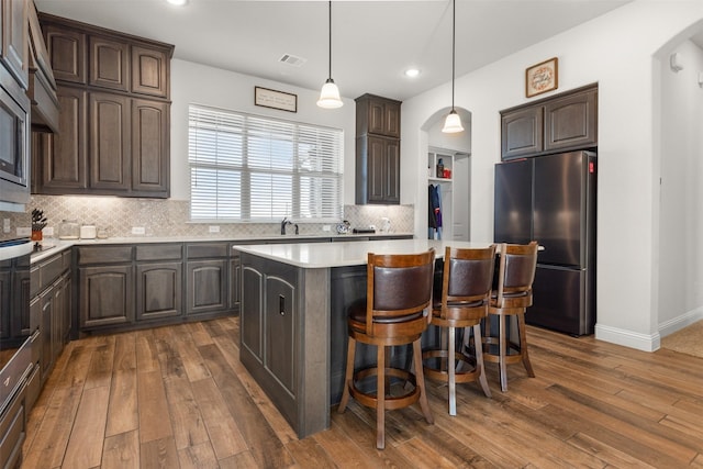 kitchen with decorative backsplash, dark brown cabinets, stainless steel fridge, and a kitchen island