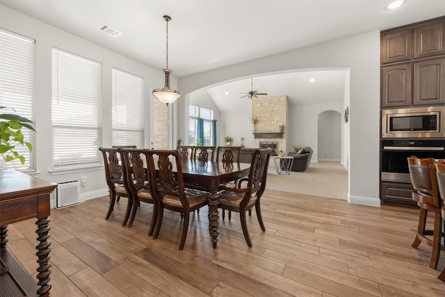 dining room featuring vaulted ceiling, ceiling fan, a fireplace, and light hardwood / wood-style floors