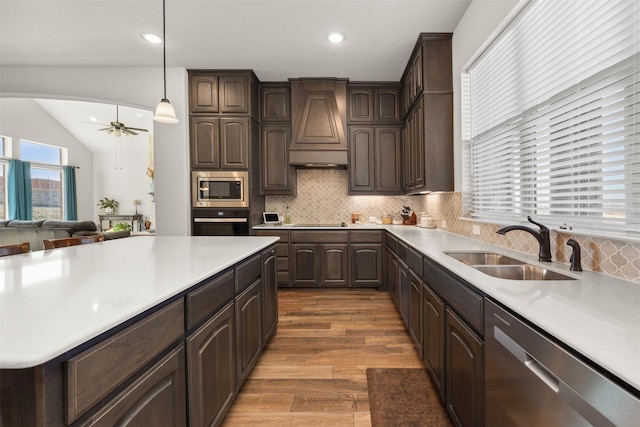 kitchen with pendant lighting, sink, premium range hood, appliances with stainless steel finishes, and vaulted ceiling