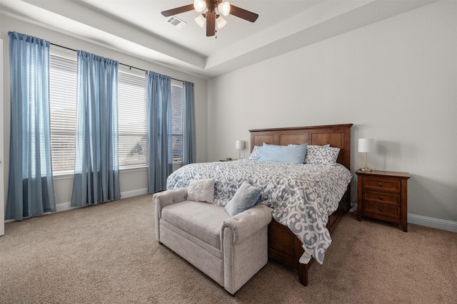 carpeted bedroom with multiple windows, a raised ceiling, and ceiling fan