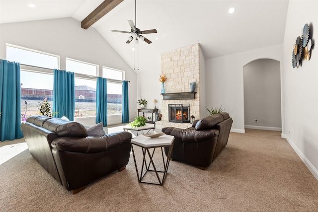 living room with ceiling fan, beam ceiling, high vaulted ceiling, light carpet, and a stone fireplace