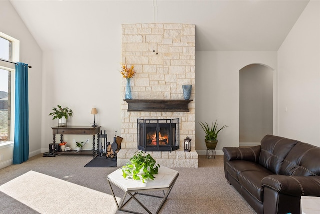 carpeted living room featuring a stone fireplace and vaulted ceiling