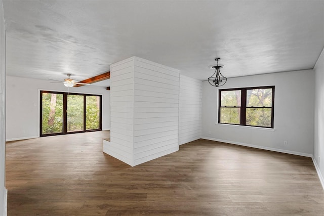 unfurnished living room with dark hardwood / wood-style floors, ceiling fan with notable chandelier, and beam ceiling