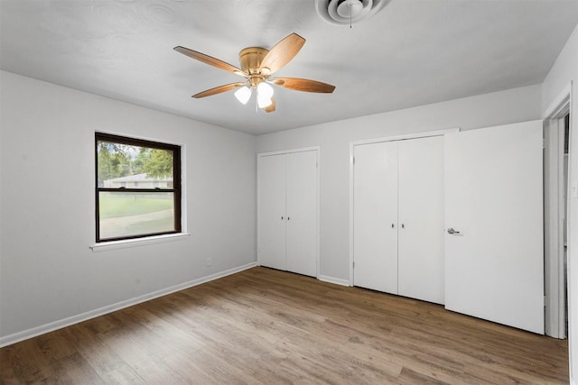 unfurnished bedroom with multiple closets, light hardwood / wood-style flooring, and ceiling fan