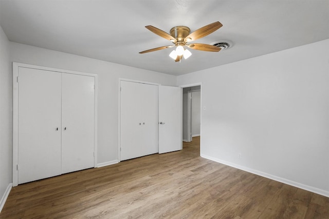 unfurnished bedroom with ceiling fan, light hardwood / wood-style flooring, and two closets