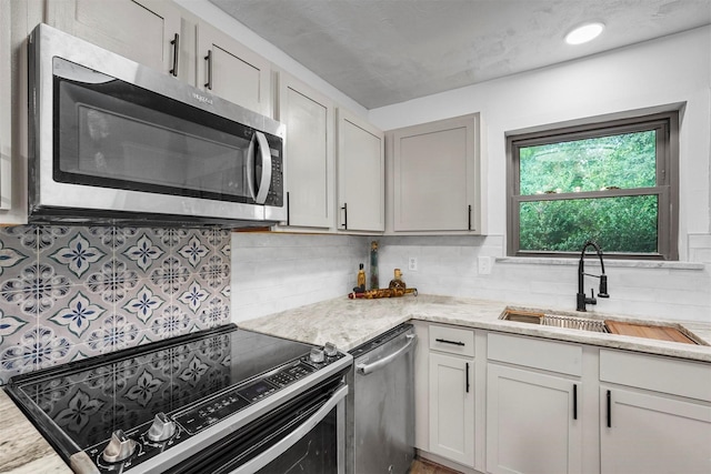 kitchen with light stone counters, sink, decorative backsplash, and stainless steel appliances