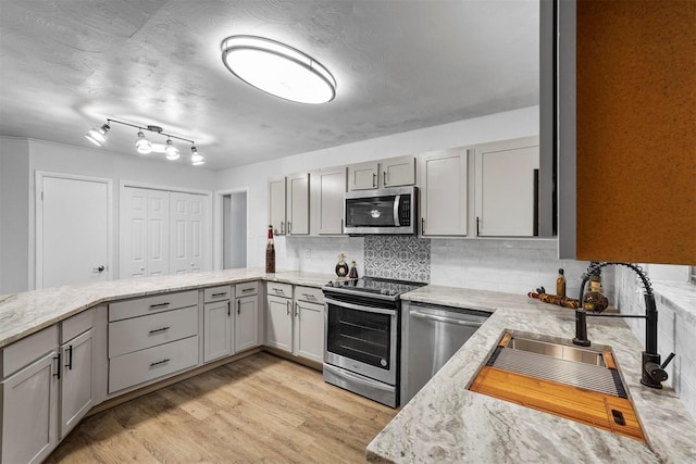 kitchen featuring gray cabinets, appliances with stainless steel finishes, light stone countertops, decorative backsplash, and light wood-type flooring