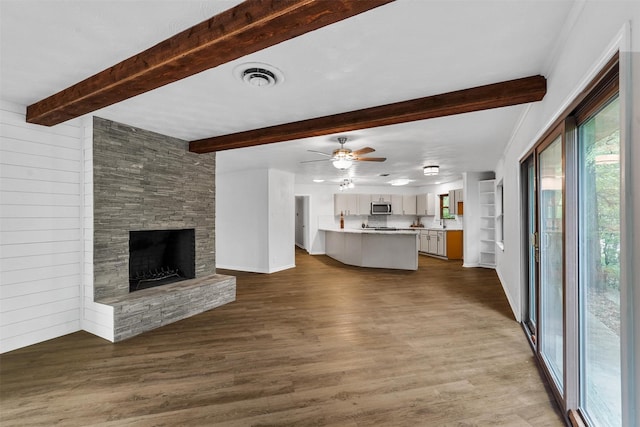 unfurnished living room featuring ceiling fan, a fireplace, built in features, and wood-type flooring