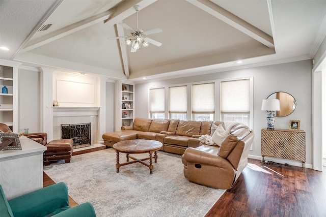 living room with a tile fireplace, ceiling fan, hardwood / wood-style floors, lofted ceiling with beams, and built in shelves