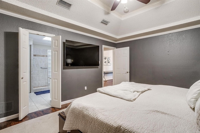 bedroom with ensuite bathroom, wood-type flooring, ornamental molding, ceiling fan, and a tray ceiling