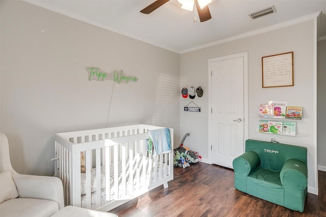 bedroom featuring a nursery area, ceiling fan, ornamental molding, and dark hardwood / wood-style floors