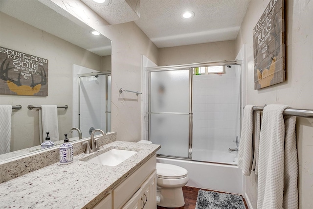 full bathroom featuring hardwood / wood-style flooring, vanity, enclosed tub / shower combo, toilet, and a textured ceiling