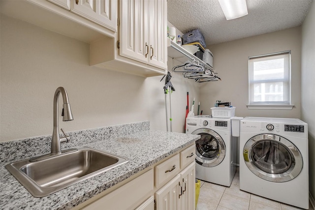 clothes washing area with washing machine and clothes dryer, sink, cabinets, a textured ceiling, and light tile patterned floors