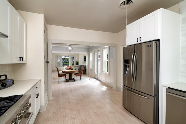 kitchen with hanging light fixtures, stainless steel appliances, light hardwood / wood-style floors, and white cabinets