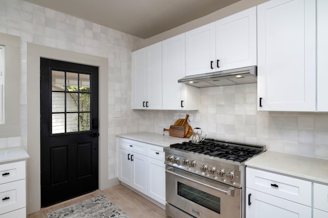 kitchen featuring tasteful backsplash, light stone counters, light hardwood / wood-style floors, high end stove, and white cabinets