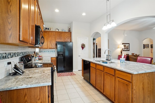 kitchen featuring sink, decorative light fixtures, black appliances, a center island with sink, and backsplash