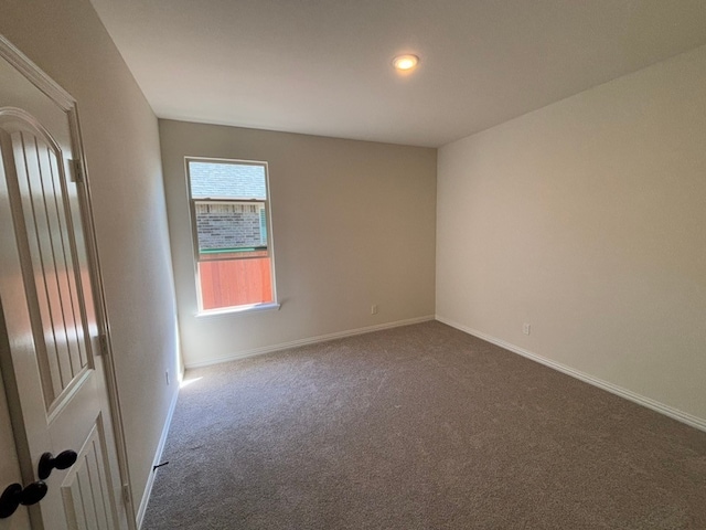 spare room with baseboards and dark carpet