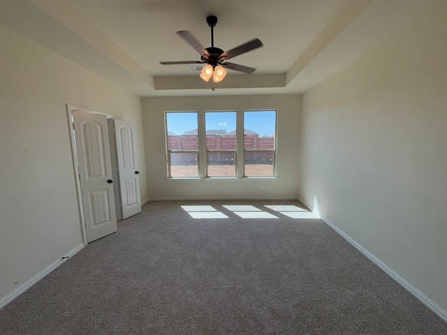 unfurnished room with ceiling fan, baseboards, carpet, and a tray ceiling