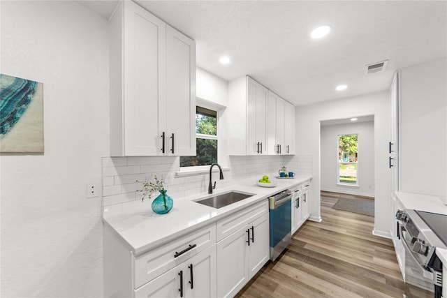 kitchen featuring sink, stainless steel appliances, white cabinets, decorative backsplash, and light wood-type flooring