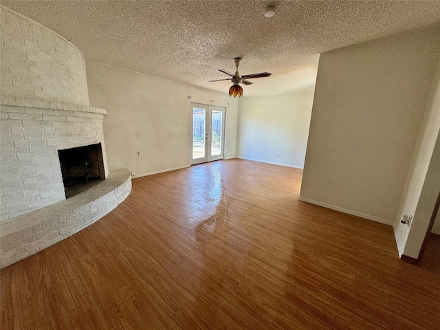 unfurnished living room with hardwood / wood-style floors, a fireplace, ceiling fan, a textured ceiling, and french doors