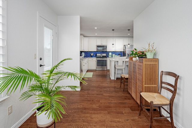 interior space with white cabinets, dark wood-style floors, appliances with stainless steel finishes, decorative light fixtures, and light countertops