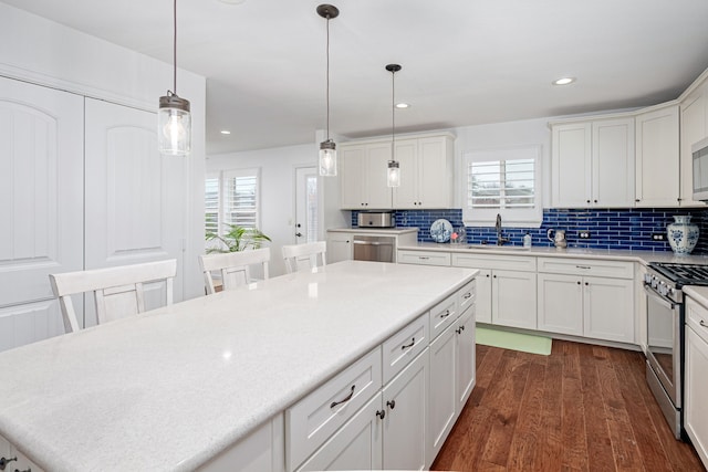 kitchen with stainless steel appliances, a sink, white cabinets, light countertops, and decorative light fixtures