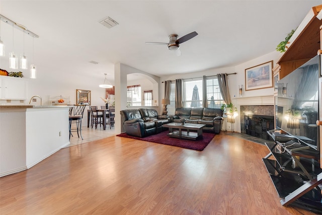 living room featuring ceiling fan, sink, a fireplace, and light hardwood / wood-style floors