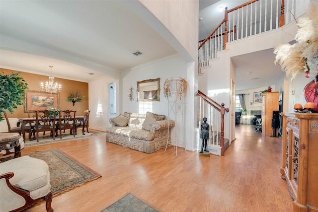 living room with light wood-type flooring, a chandelier, crown molding, and a towering ceiling