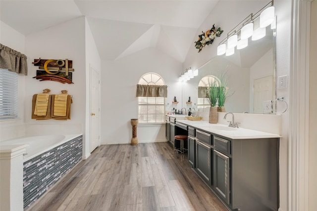 bathroom featuring tiled bath, lofted ceiling, wood-type flooring, and vanity