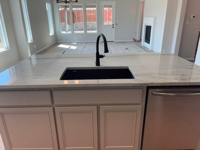 kitchen with a sink, light stone countertops, dishwasher, and a fireplace with flush hearth