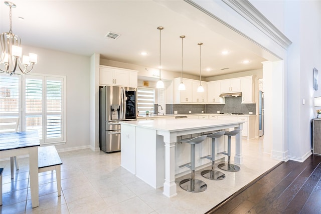 kitchen with hanging light fixtures, white cabinets, a kitchen island, stainless steel fridge with ice dispenser, and decorative backsplash