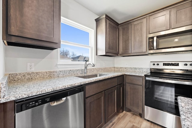 kitchen with sink, dark brown cabinets, stainless steel appliances, light stone countertops, and light wood-type flooring