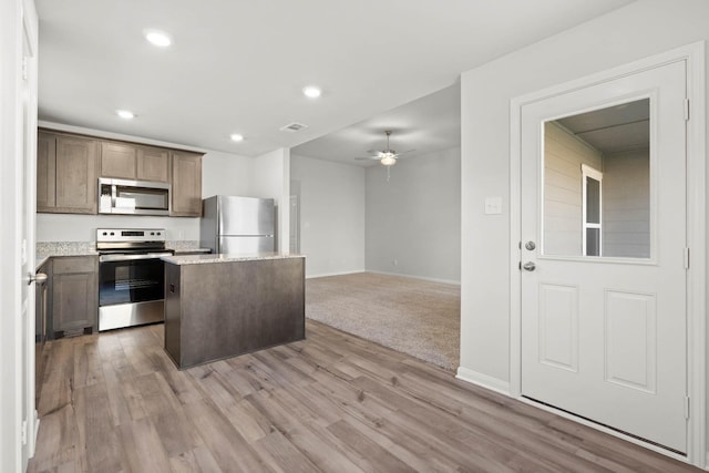 kitchen with appliances with stainless steel finishes, a center island, ceiling fan, and light wood-type flooring