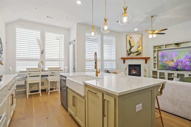 kitchen featuring pendant lighting, an island with sink, a kitchen bar, stainless steel dishwasher, and light hardwood / wood-style flooring