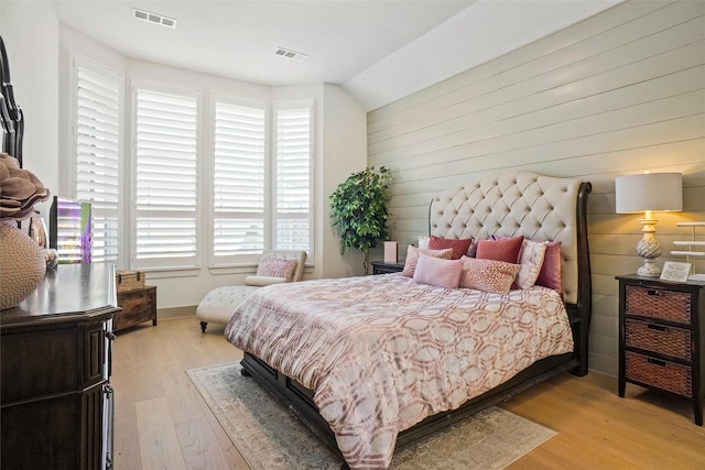 bedroom featuring lofted ceiling, wooden walls, and light hardwood / wood-style floors