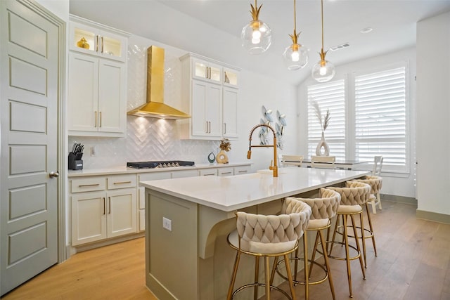 kitchen featuring wall chimney range hood, decorative backsplash, decorative light fixtures, and a center island with sink