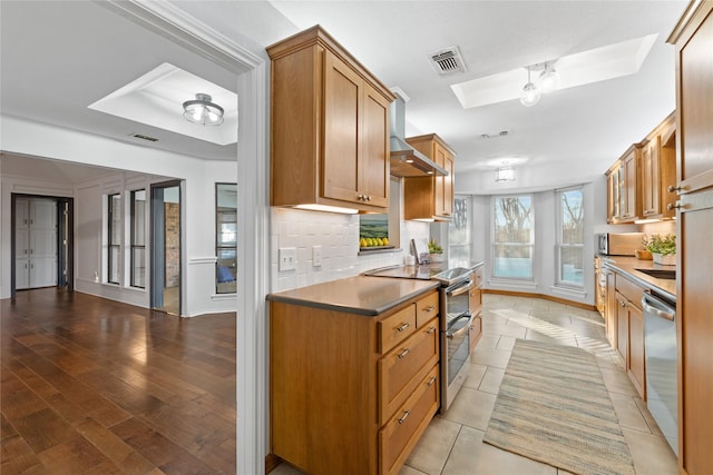 kitchen featuring a skylight, light hardwood / wood-style floors, wall chimney exhaust hood, and appliances with stainless steel finishes