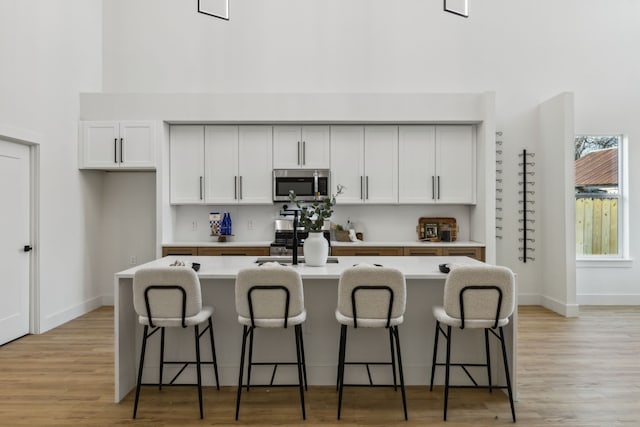 kitchen with stainless steel appliances, a center island with sink, white cabinets, and a kitchen breakfast bar