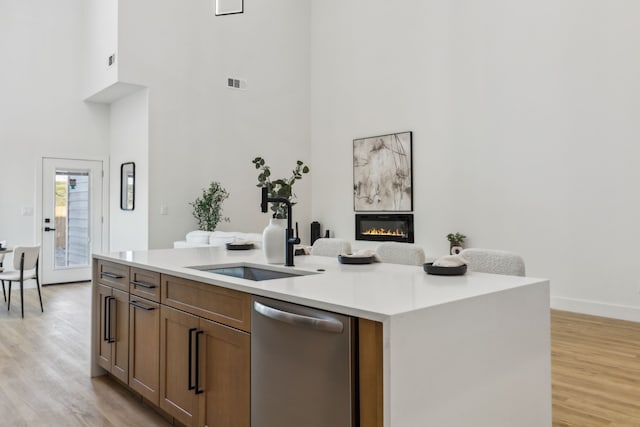 kitchen featuring sink, dishwasher, a kitchen island with sink, a towering ceiling, and light hardwood / wood-style floors