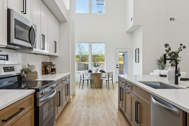 kitchen featuring a towering ceiling, stainless steel appliances, sink, and white cabinets