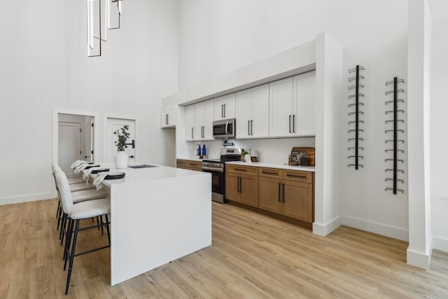 kitchen featuring appliances with stainless steel finishes, a breakfast bar, white cabinetry, a center island, and light wood-type flooring