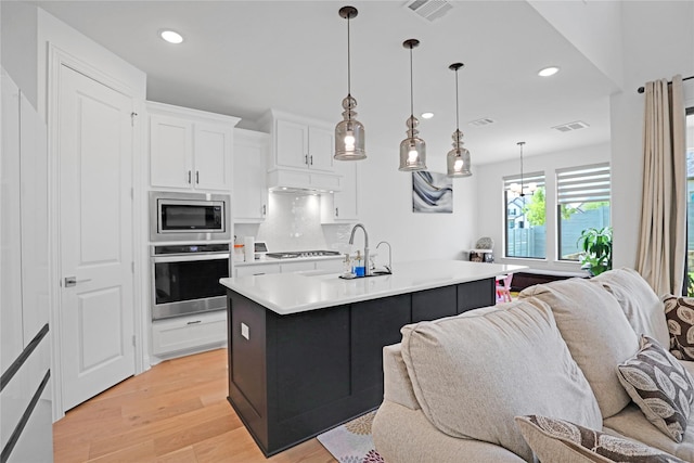 kitchen featuring stainless steel appliances, an island with sink, white cabinetry, and decorative light fixtures