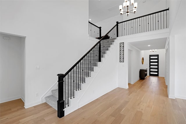 staircase featuring a high ceiling, wood-type flooring, and an inviting chandelier