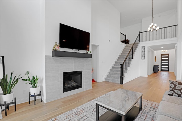 living room featuring a high ceiling, a tiled fireplace, hardwood / wood-style floors, and a notable chandelier