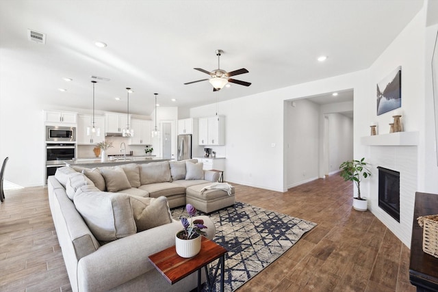 living room featuring a tiled fireplace, sink, and ceiling fan