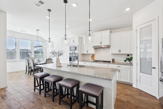 kitchen with a breakfast bar area, stainless steel appliances, white cabinets, a center island with sink, and decorative light fixtures