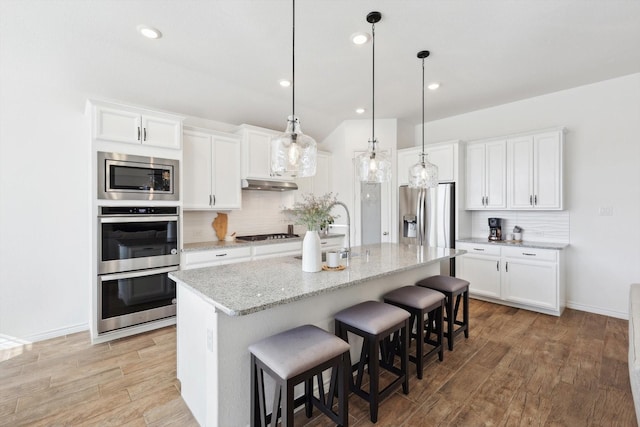 kitchen featuring white cabinetry, appliances with stainless steel finishes, an island with sink, and light stone counters