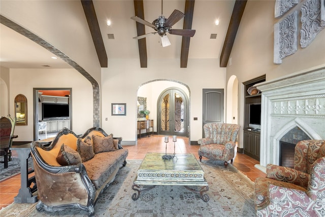 tiled living room featuring built in features, beamed ceiling, ceiling fan, a fireplace, and a high ceiling