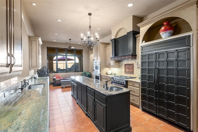 kitchen featuring pendant lighting, light tile patterned floors, light stone counters, and a center island with sink