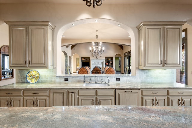 kitchen featuring light brown cabinetry, sink, decorative backsplash, hanging light fixtures, and an inviting chandelier